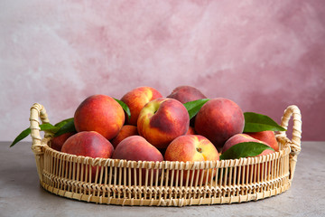 Fototapeta na wymiar Wicker tray with tasty peaches on grey table against pink background