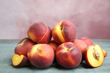 Pile of ripe peaches on blue wooden table against pink background