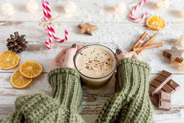 Hands of woman hold hot cup of cappuccino or hot milk chocolate with dried orange fruit and cinnamon. Christmas hot drink.