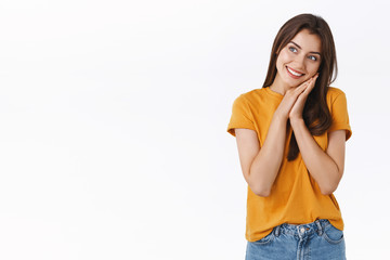 Cheerful, silly and dreamy romantic woman in yellow t-shirt, leaning face on palms and looking sideways with pleased, thoughtful expression, smiling, dreaming about something, white background