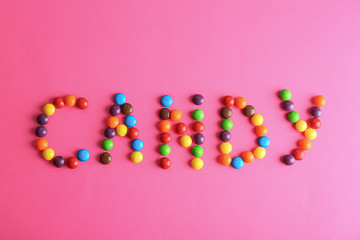 Word CANDY made of different glazed candies on pink background, flat lay