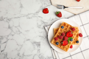 Flat lay composition with delicious waffles and fresh berries on white marble table. Space for text