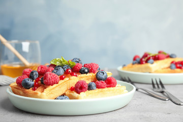Delicious waffles with fresh berries served on grey table against blue background. Space for text