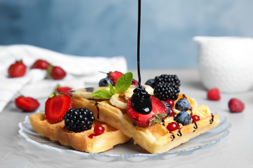 Pouring sauce onto delicious waffles with fresh berries served on grey table