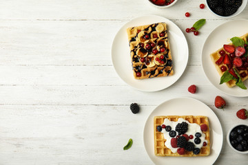 Flat lay composition with delicious waffles and fresh berries on white wooden table. Space for text