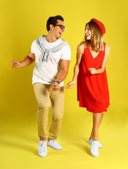 Beautiful young couple dancing on yellow background
