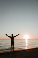 Fototapeta na wymiar Silhouette of a young man enjoying beautiful sunset on the beach 