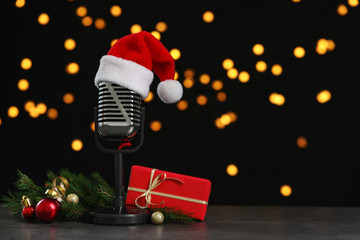 Microphone with Santa hat and decorations on grey table against blurred lights, space for text....