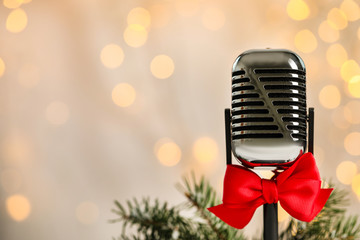 Fototapeta na wymiar Microphone with red bow and fir branches against blurred lights, space for text. Christmas music