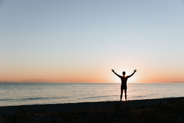 Fototapeta premium Silhouette of a young man enjoying beautiful sunset on the beach 