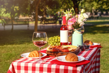 Wine, food and flowers on picnic table in park on sunny day