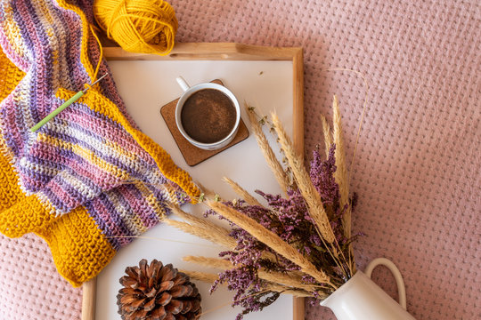 Fall Layout With An Infinity Scarf In Double Crochet Pattern On A Wooden Tray Next To A Ball Of Yarn, A Cup Of Coffee And A Vintage Vase With Dried Summer Wildflowers. DIY Fashion Project.