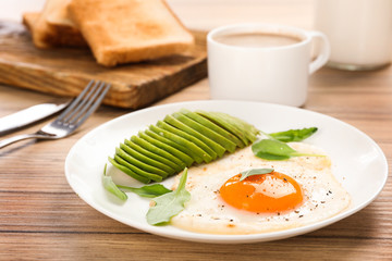 Tasty breakfast with fried egg and avocado on wooden table, closeup
