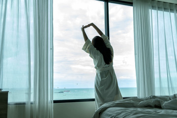 Behide asian woman in bathrobe suit open curtain to see view outside in morning, Travel and Holiday concept