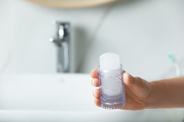 Woman holding crystal alum deodorant in bathroom, closeup. Space for text
