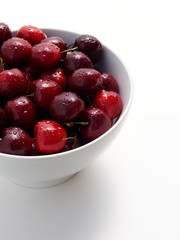 A bowl full of freshly washed cherries on white.