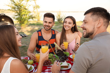 Happy young people having picnic at table in park