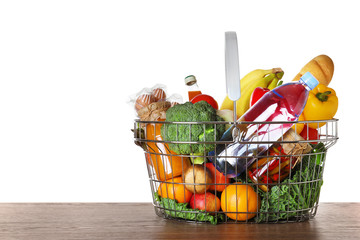 Shopping basket with grocery products on wooden table against white background. Space for text