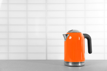 Stylish electric kettle on grey table against white wall, space for text. Tea preparation
