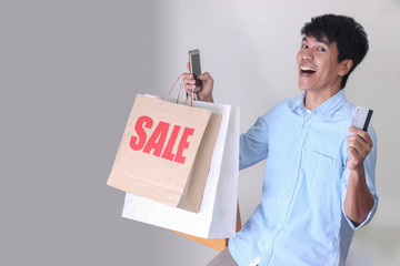 Asian  smilely man holding paper shopping bag and smart phone.