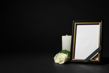 Funeral photo frame with ribbon, white rose and candle on dark table against black background....