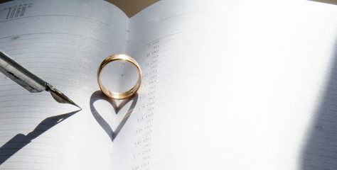 A golden ring in the middle of an open diary. Shadow in the shape of a heart. Nearby is a vintage fountain pen. Concept - Valentine's Day