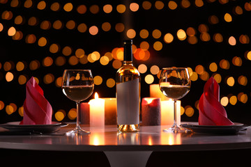 Romantic table setting with bottle of wine and burning candles against blurred background