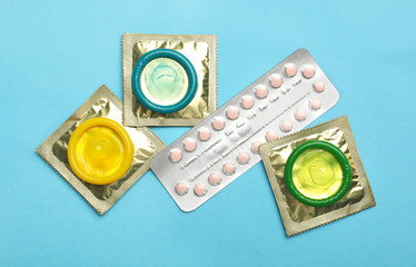 Condoms and birth control pills on light blue background, flat lay. Safe sex concept