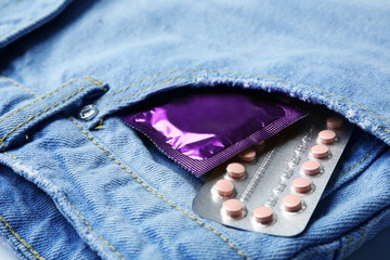 Purple condom and birth control pills in pocket of jeans, closeup. Safe sex concept