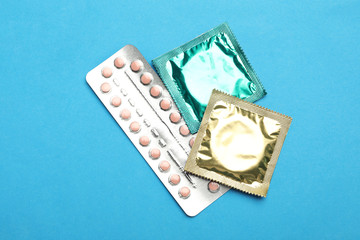 Condoms and birth control pills on light blue background, flat lay. Safe sex concept
