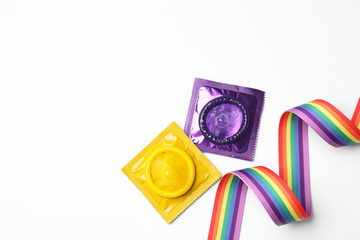 Colorful condoms and rainbow ribbon on white background, top view. LGBT concept