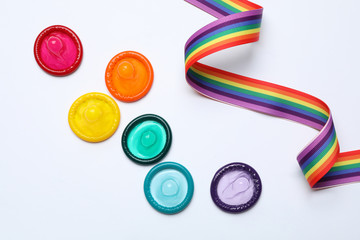 Colorful condoms and rainbow ribbon on white background, top view. LGBT concept - obrazy, fototapety, plakaty