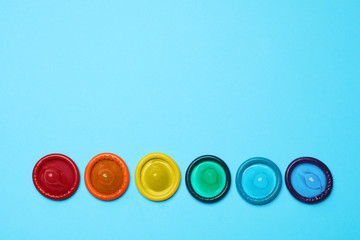 Colorful condoms on light blue background, flat lay. LGBT concept