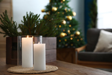 Burning candles and fir branches on wooden table in room decorated for Christmas