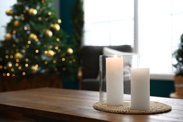 Burning candles on wooden table in room decorated for Christmas