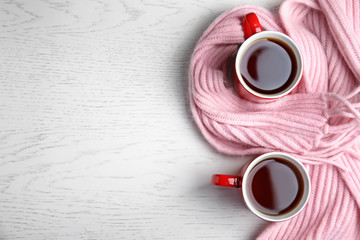 Flat lay composition cups of hot tea and knitted scarf on white wooden background, space for text. Winter drink