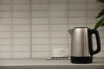 Modern electric kettle and cup on grey kitchen counter. Space for text
