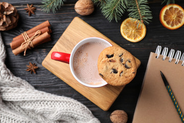 Flat lay composition with cup of tasty cocoa and cookie on black wooden table