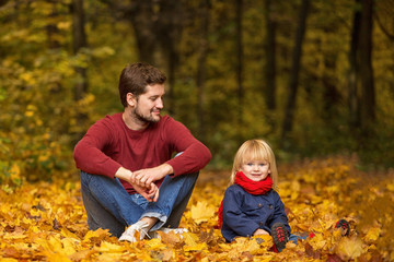 Father and daughter are sitting and laughing in an autumn park.