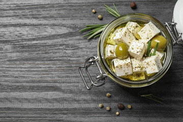 Pickled feta cheese in jar on grey wooden table, top view. Space for text