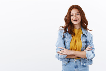 Fototapeta premium Lifestyle, fashion and women concept. Cheerful ambitious redhead woman in denim jacket cross arms in confident pose, smiling accomplished and self-assured, standing white background
