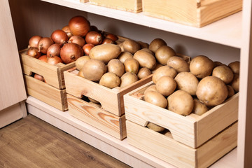 Crates with potatoes and onions on shelf. Orderly storage