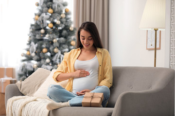 Happy pregnant woman with Christmas gift box at home. Expecting baby