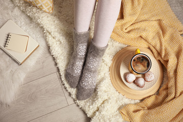 Woman and cup of hot winter drink on floor at home, above view