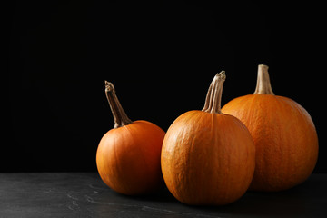 Ripe pumpkins on grey table against black background, space for text. Holiday decoration