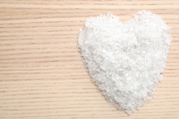 Heart made of white sea salt on wooden background, top view with space for text. Spa treatment