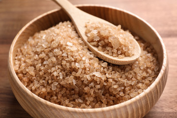 Bowl and spoon with brown sea salt on wooden table, closeup. Spa treatment