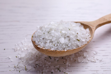 Spoon with sea salt on white wooden table, closeup. Spa treatment
