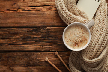 Flat lay composition with cup of coffee and knitted scarf on wooden table, space for text. Cozy...