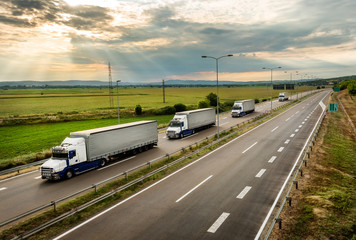 Lorry trucks in line as a caravan or convoy  on country highway under a beautiful sky